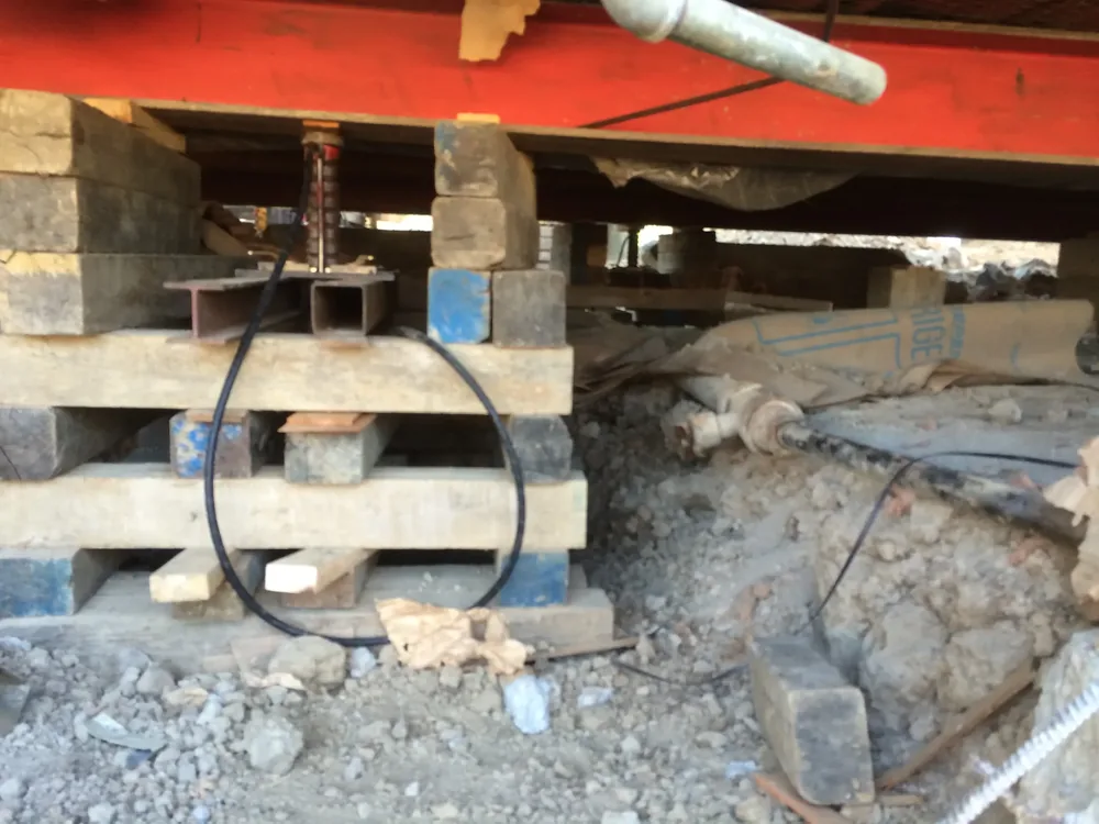 Hydraulic jack on timber cribbing lifting a steel beam beneath a home during leveling