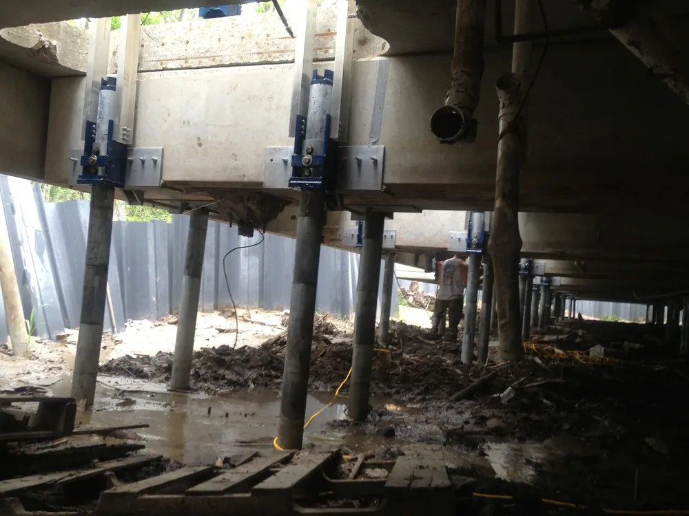 Concrete support piers capped with heavy blue steel underpinning brackets beneath a leveled home